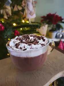 Glass mug of Black Forest hot chocolate topped with whipped cream and chocolate shavings in front of a Christmas tree.