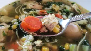 Homemade chicken noodle soup with carrots, celery, corn, cauliflower, and tender chicken in a clear broth.