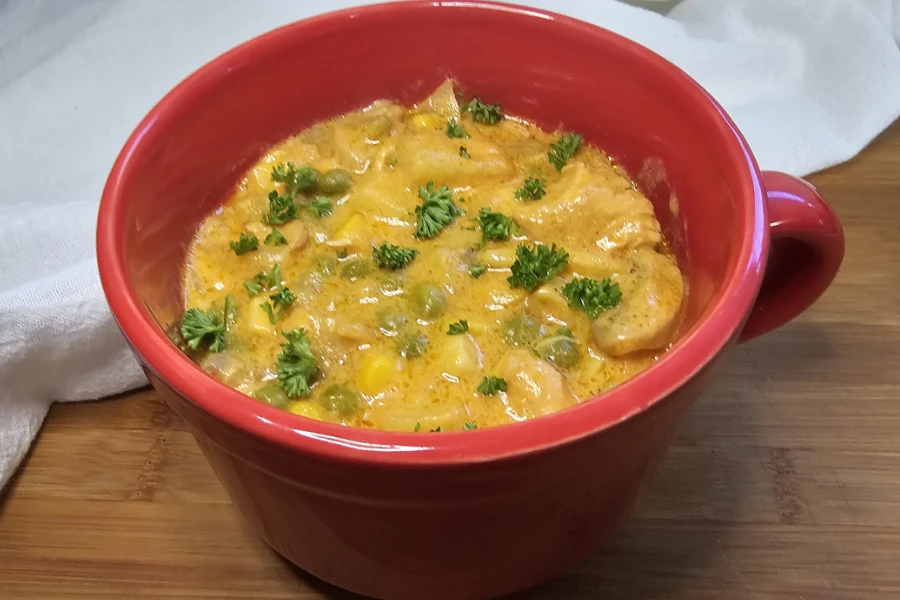Creamy chicken curry soup with peas and corn topped with chopped parsley in a red soup mug