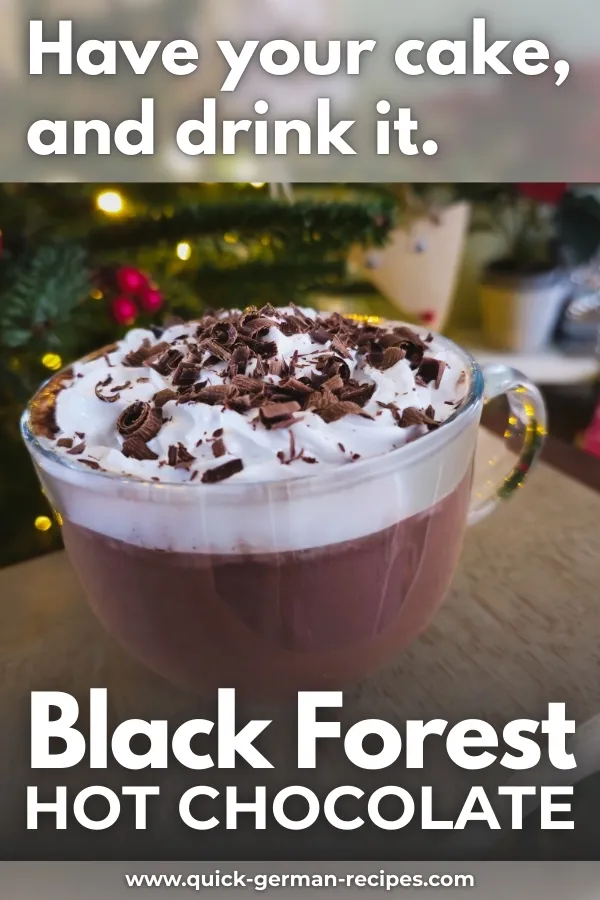 Glass mug of Black Forest hot chocolate topped with whipped cream and chocolate shavings in front of a Christmas tree.