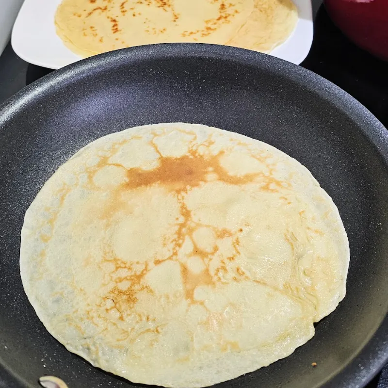 Cooking crêpes for asparagus and ham rolls Thin crepe cooking in a skillet until lightly set
