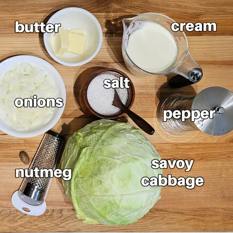 Savoy cabbage recipe ingredients Savoy cabbage, cream, butter, onion, salt, and nutmeg arranged on a wooden board for German creamed cabbage