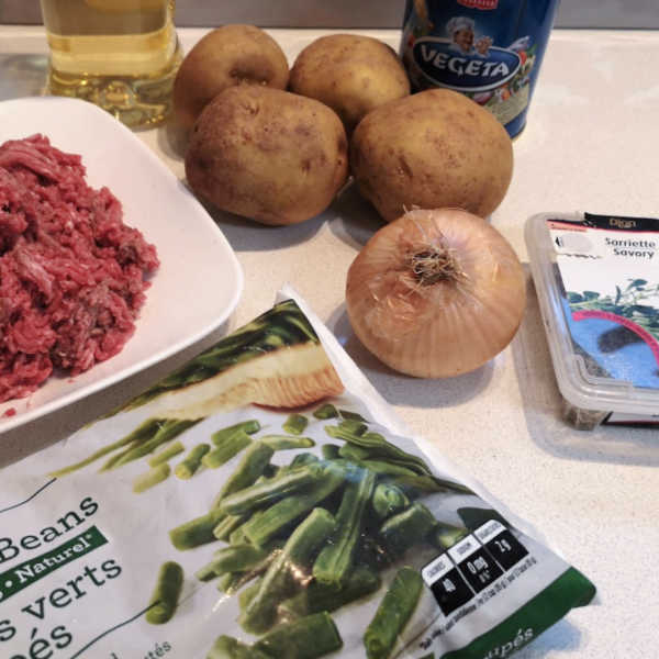 Ingredients for German green bean soup including potatoes, onion, ground beef, green beans, and seasonings on a kitchen counter.