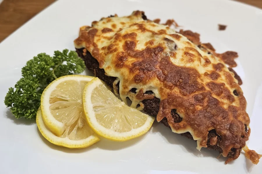 Hawaiian chicken schnitzel with melted cheese and cranberry sauce, served with lemon and parsley