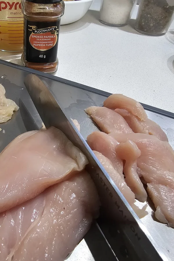 Slicing boneless chicken breasts into thin strips, with smoked paprika in the background