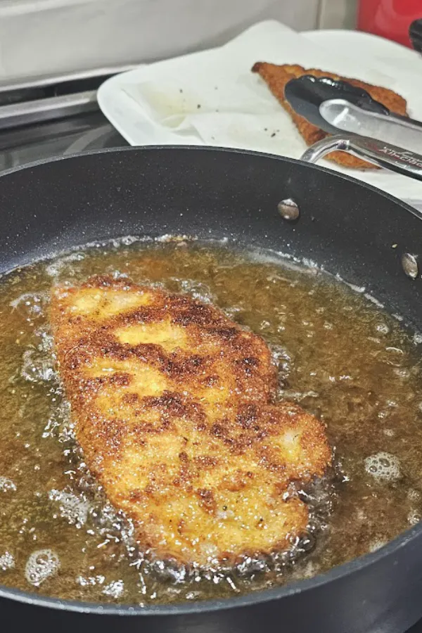 Breaded chicken schnitzel frying until golden brown in hot oil in a skillet