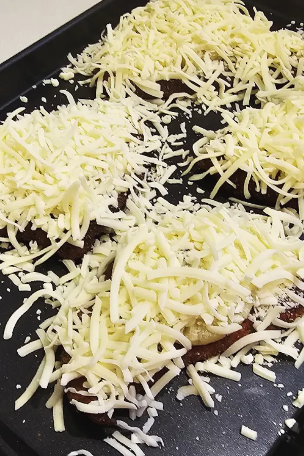 Chicken schnitzels piled with shredded cheese on a baking sheet, ready for the broiler