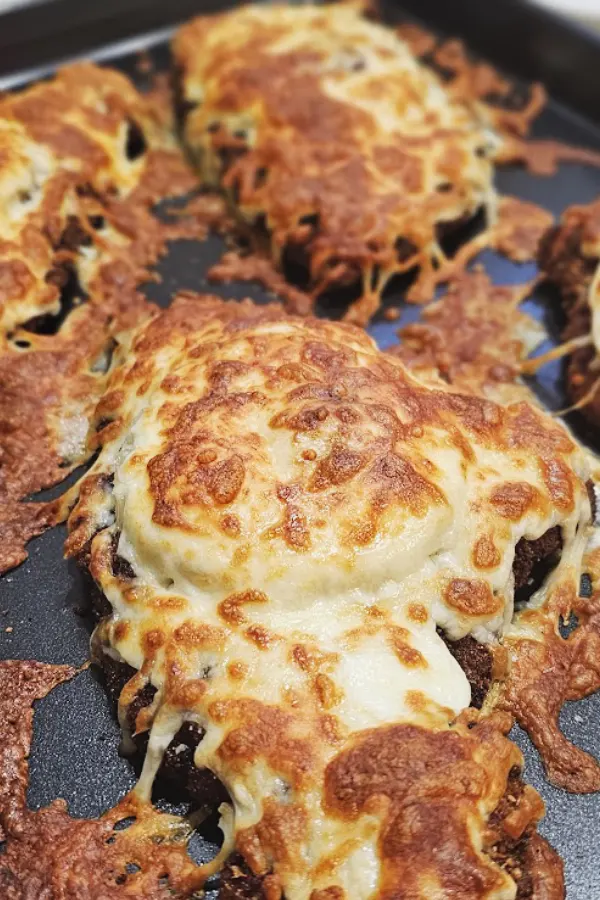 Broiled chicken schnitzels on a baking sheet with melted, browned cheese running onto the pan