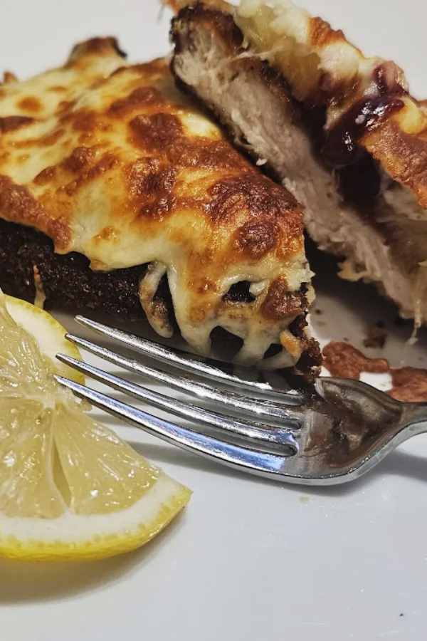 Hawaiian chicken schnitzel with melted cheese and cranberry sauce, served with lemon and parsley