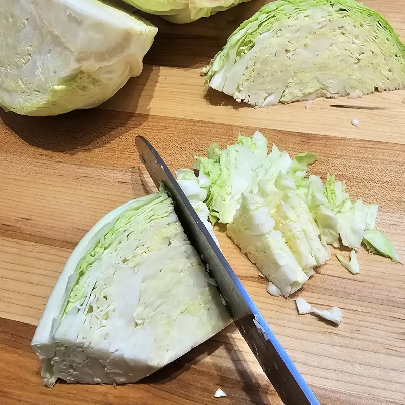 Slice the Savoy cabbage Slicing a head of Savoy cabbage into thin strips on a wooden cutting board.
