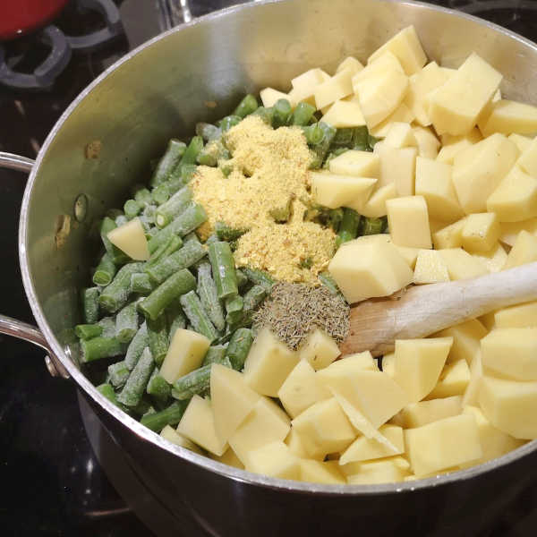 Chopped potatoes, frozen green beans, soup seasoning, and savory herb added to browned meat in a large pot.