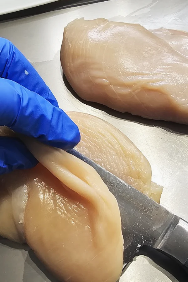 Slicing a chicken breast in half horizontally with a chef’s knife to make thin cutlets