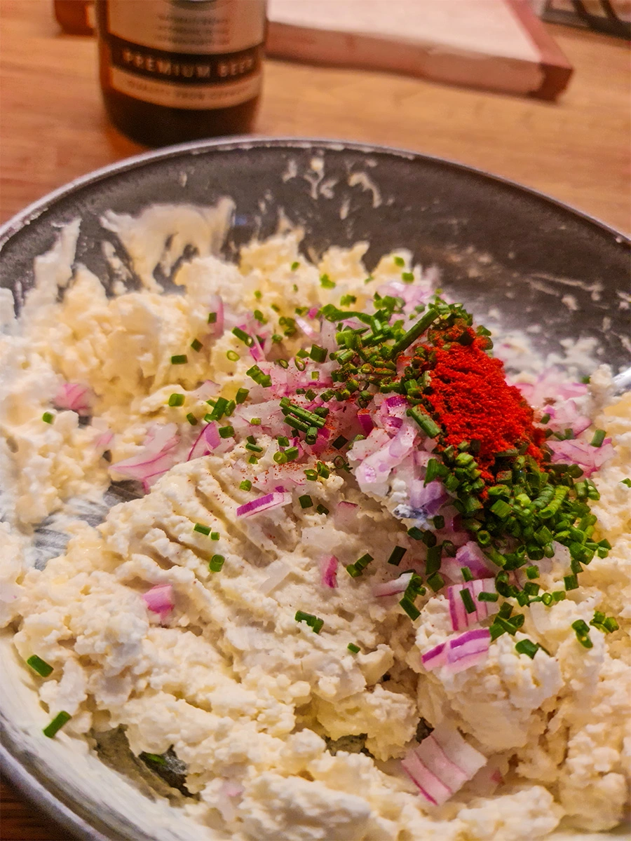 Mashed cheese mixture topped with chopped red onion, chives, and paprika for making Obatzda.