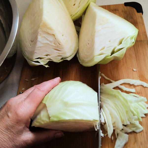 Shredding the cabbage quarters Hand holding a wedge of cabbage and slicing it into thin shreds on a cutting board, with additional cabbage pieces nearby.