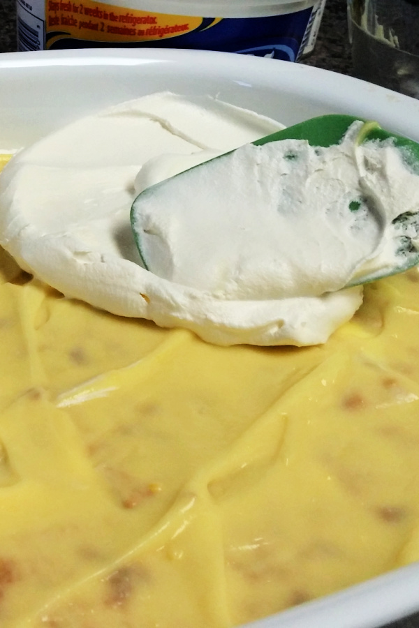 Whipped topping being spread over the vanilla pudding with a green spatula.