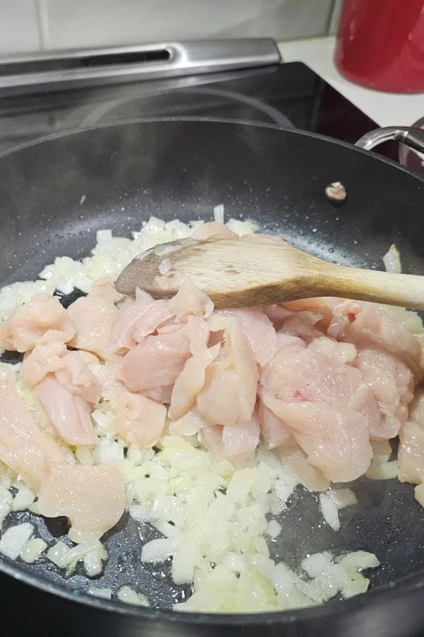 Raw chicken strips added to softened chopped onion in a large skillet