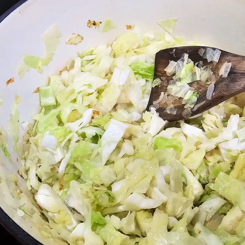 Shredded Savoy cabbage added to sautéed onions in a pot. Shredded Savoy cabbage added to sautéed onions in a pot.
