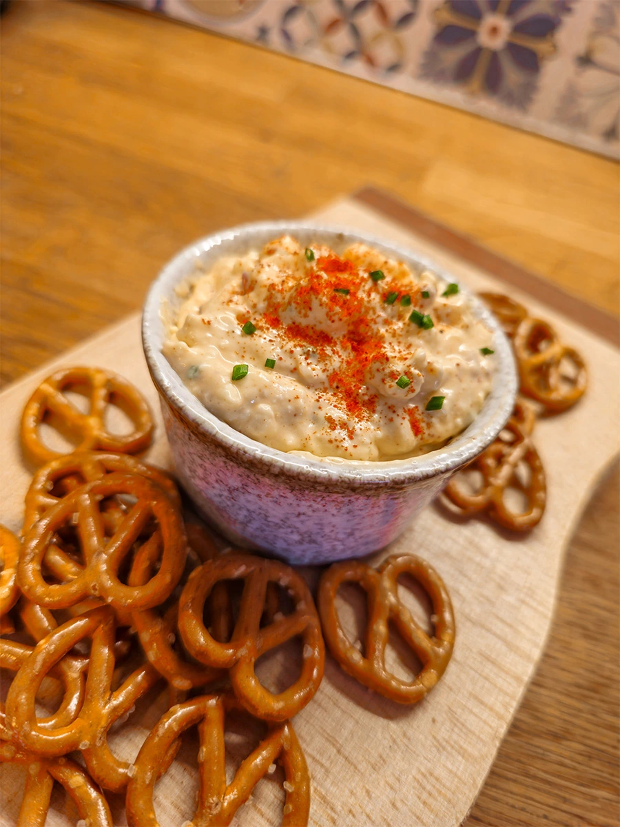 Bowl of Obatzda Bavarian cheese dip garnished with paprika and chives, served with pretzels.