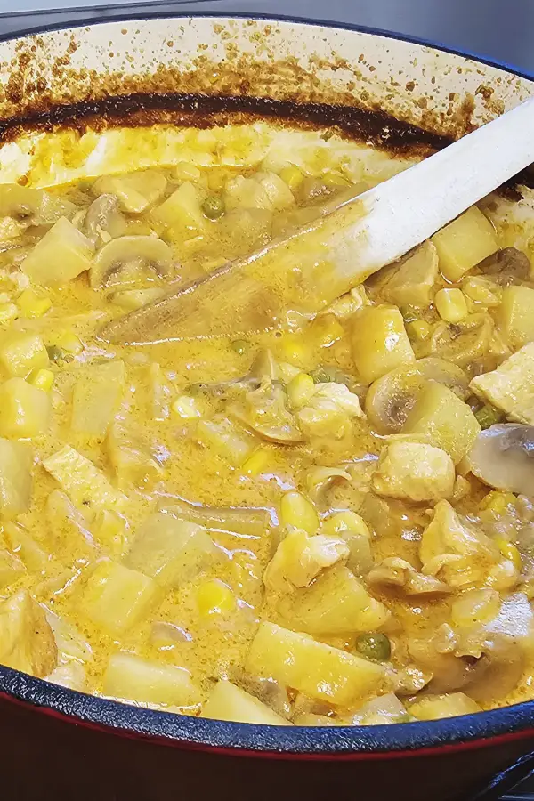 Baked German party soup in a Dutch oven with chicken, potatoes, mushrooms, corn and peas in a golden curry cream sauce