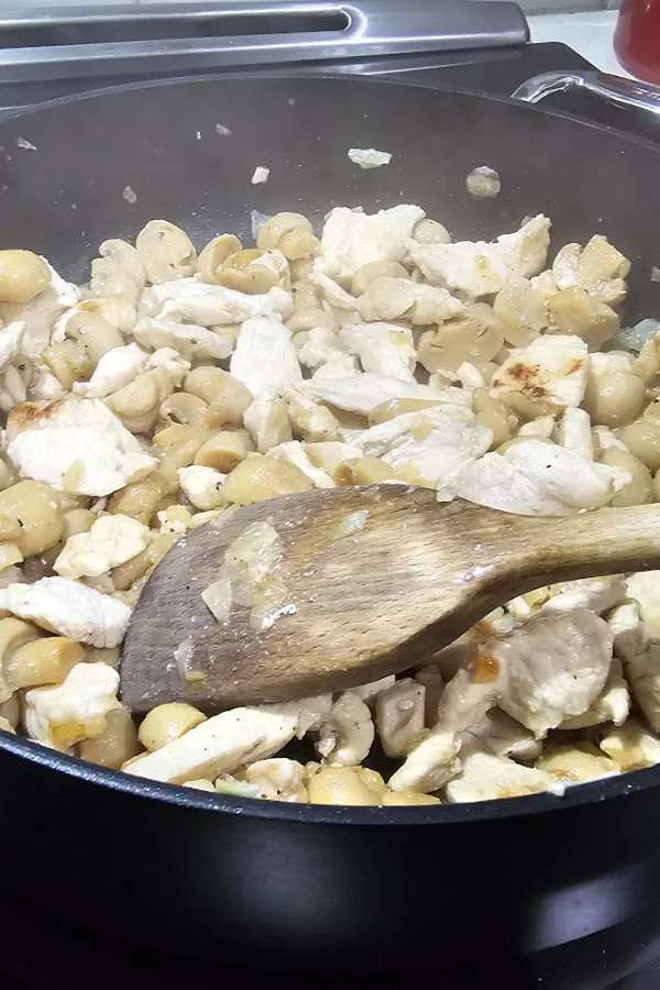 Chicken breast strips and mushrooms cooking together in a skillet for chicken stroganoff