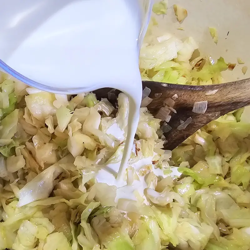 Heavy cream being poured over sautéed cabbage and onions in a cooking pot. Heavy cream being poured over sautéed cabbage and onions in a cooking pot.