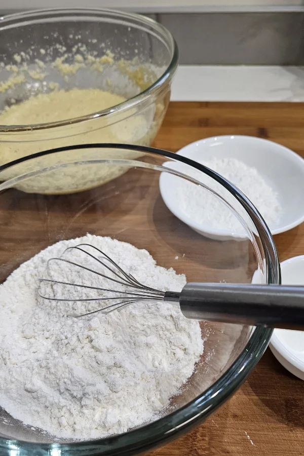 Flour, cornstarch and baking powder whisked together in a glass bowl for Amerikaner, with the creamed batter behind
