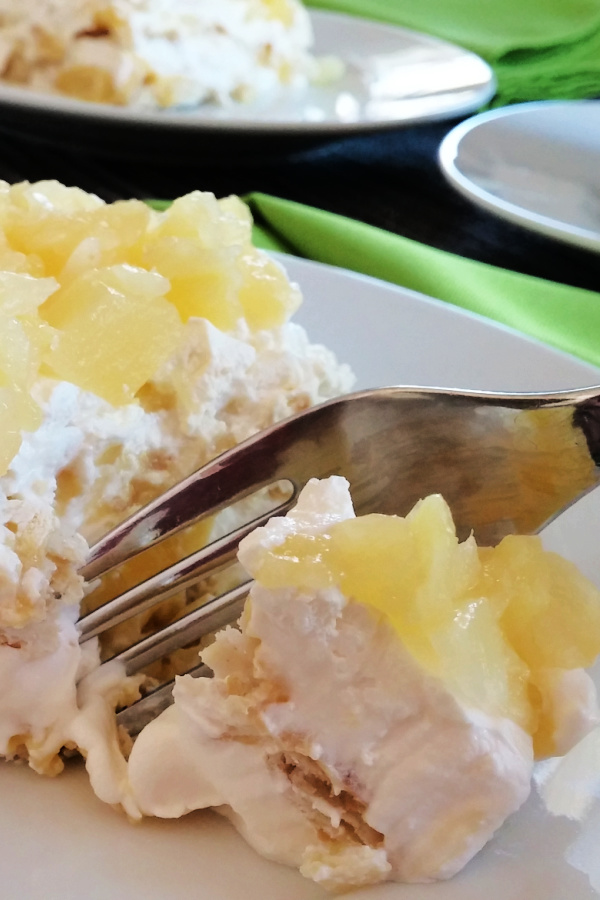 Close-up of pineapple soda cracker dessert with creamy layers and a fork beside a bite.