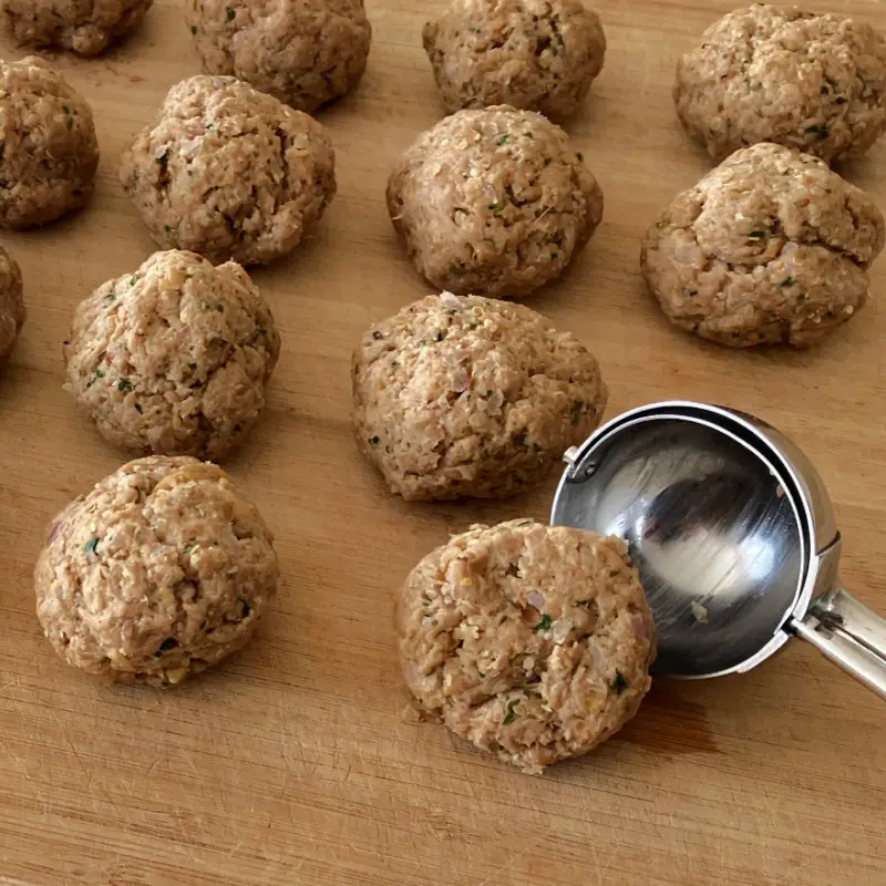 Raw vegan seitan meatballs shaped on a wooden board with a cookie scoop.