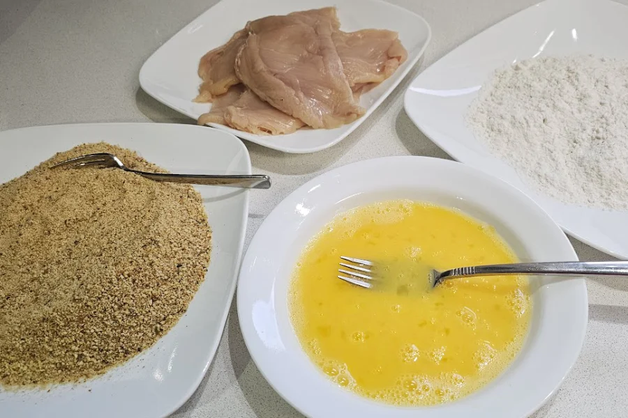 Breading station with breadcrumbs, beaten eggs, flour and thin chicken cutlets for schnitzel