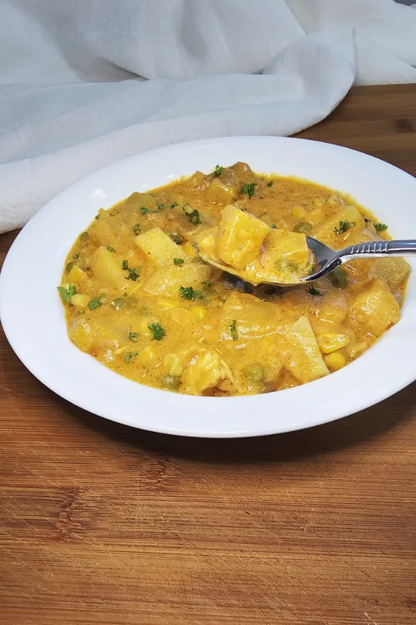 Creamy German chicken and potato soup in a white bowl, with a fork lifting a potato cube