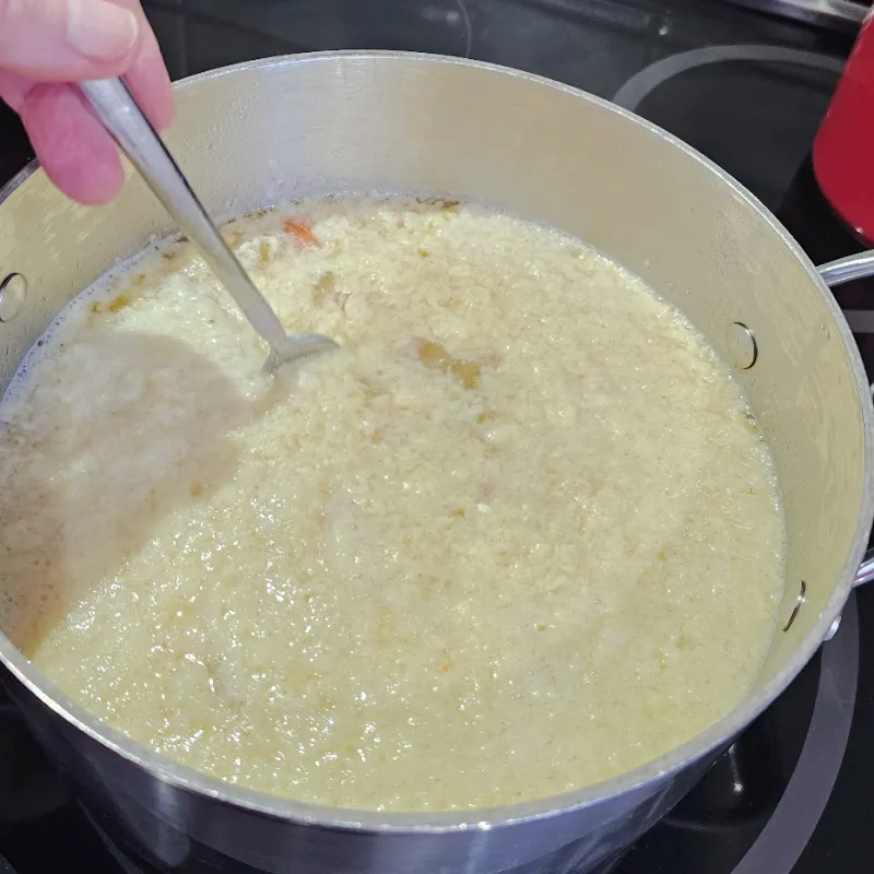 German egg drop soup (Einlaufsuppe) in a pot after adding batter, showing egg wisps forming in broth.