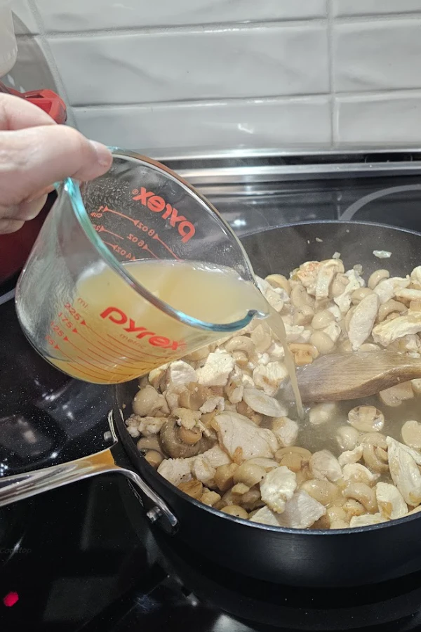 Adding chicken broth to browned chicken strips and mushrooms in a skillet