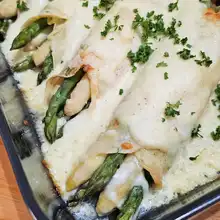 Baked asparagus and ham crêpes casserole garnished with parsley
