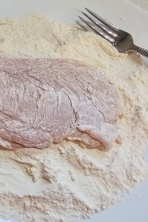 Pounded chicken cutlet coated in flour on a white plate