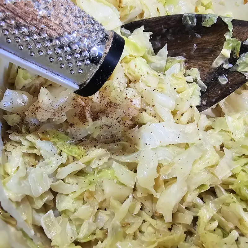 season with freshly grated nutmeg Freshly grated nutmeg being added to creamy Savoy cabbage in a pot.