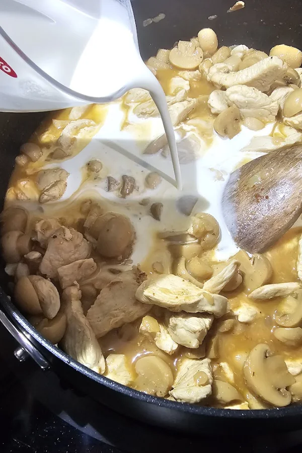 Pouring heavy cream into chicken, mushrooms and broth in a skillet for chicken stroganoff without sour cream
