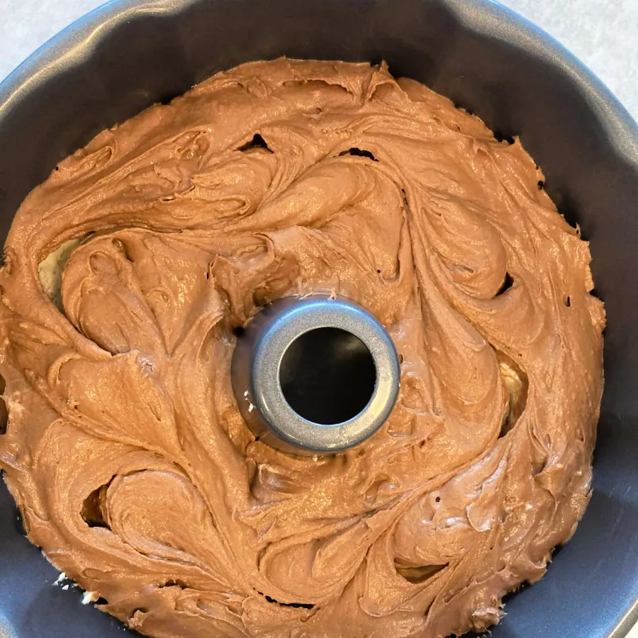 Chocolate batter spooned over vanilla batter in a Bundt pan for vegan marble cake