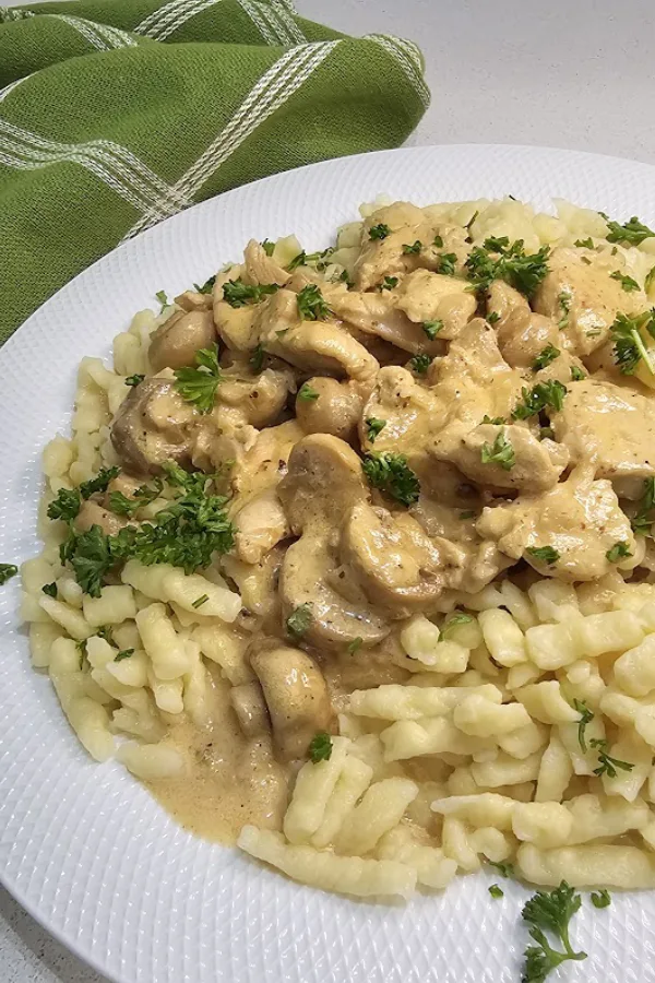 Creamy chicken stroganoff with mushrooms served over German spätzle and topped with fresh parsley