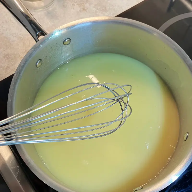 Sauce base being whisked in a saucepan until smooth and creamy.