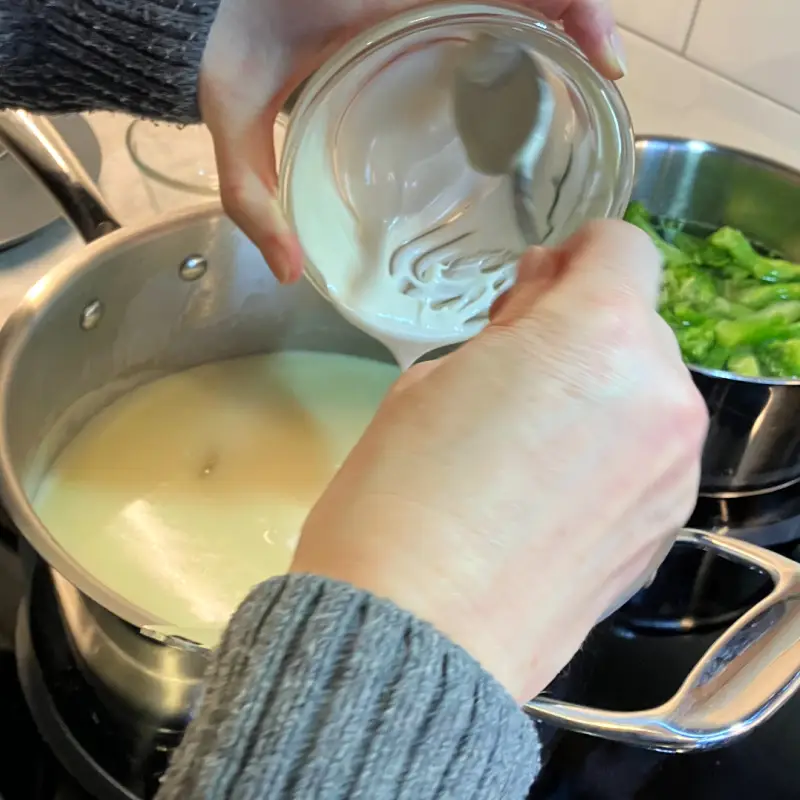 Vegan sour cream mixture being poured into a saucepan while stirring.