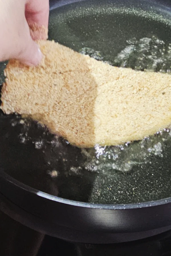 Hand laying a breaded chicken cutlet into hot oil in a nonstick skillet