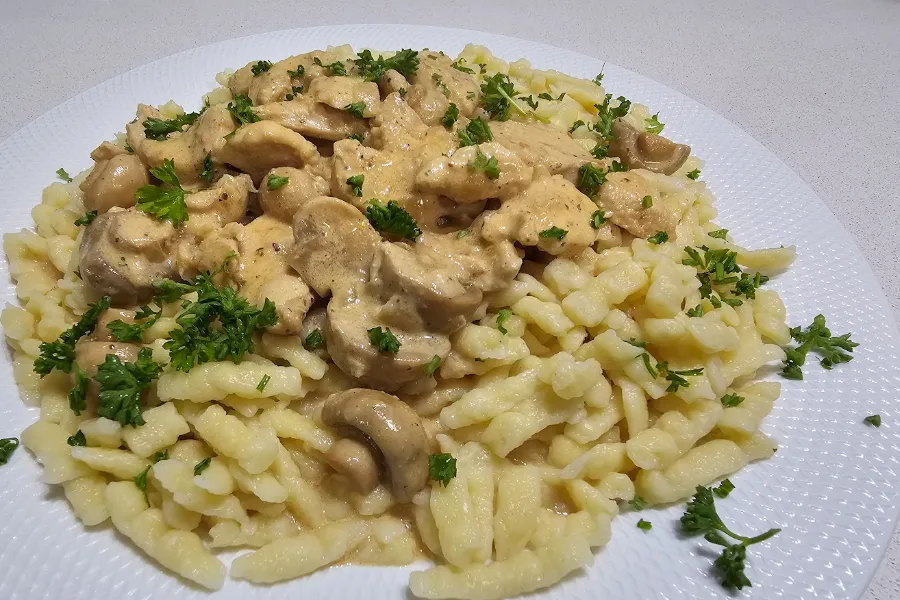Chicken stroganoff in a creamy mushroom sauce over homemade spätzle on a white plate