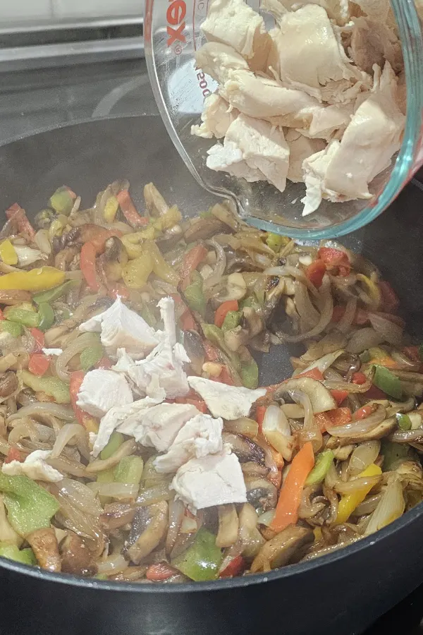 Pieces of cooked rotisserie chicken added to peppers, mushrooms and onions in a skillet