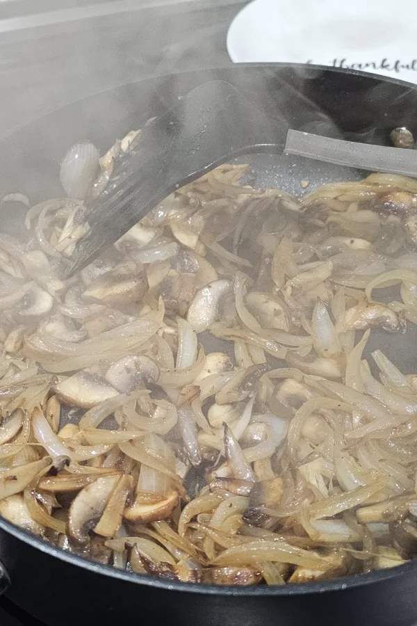 Sliced mushrooms and onions sautéing together in a steaming skillet