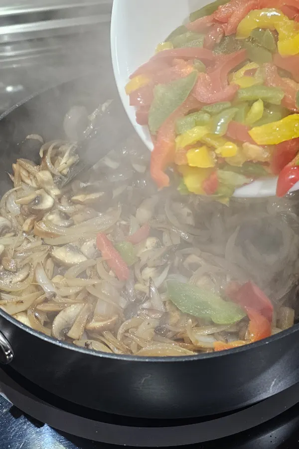Frozen red, yellow and green bell pepper strips poured into a skillet of onions and mushrooms