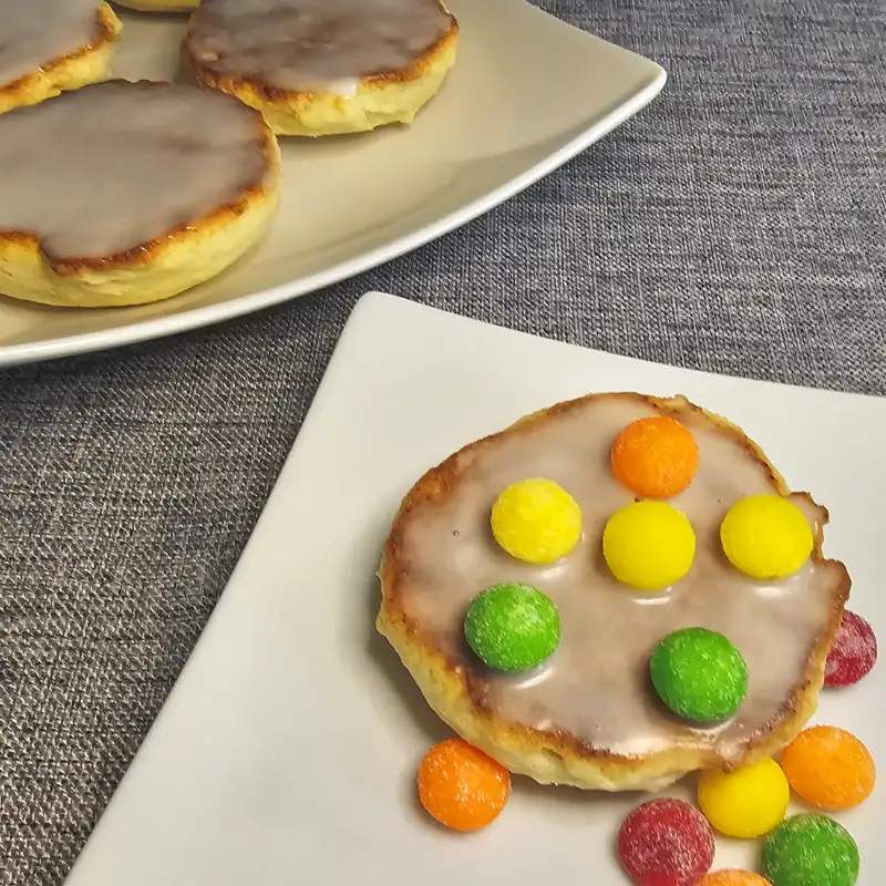 Oma's Amerikaner, soft German iced cake cookies, with one topped with colorful candies on a white plate