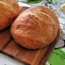 Two golden loaves of no-knead artisan bread on a wooden board.