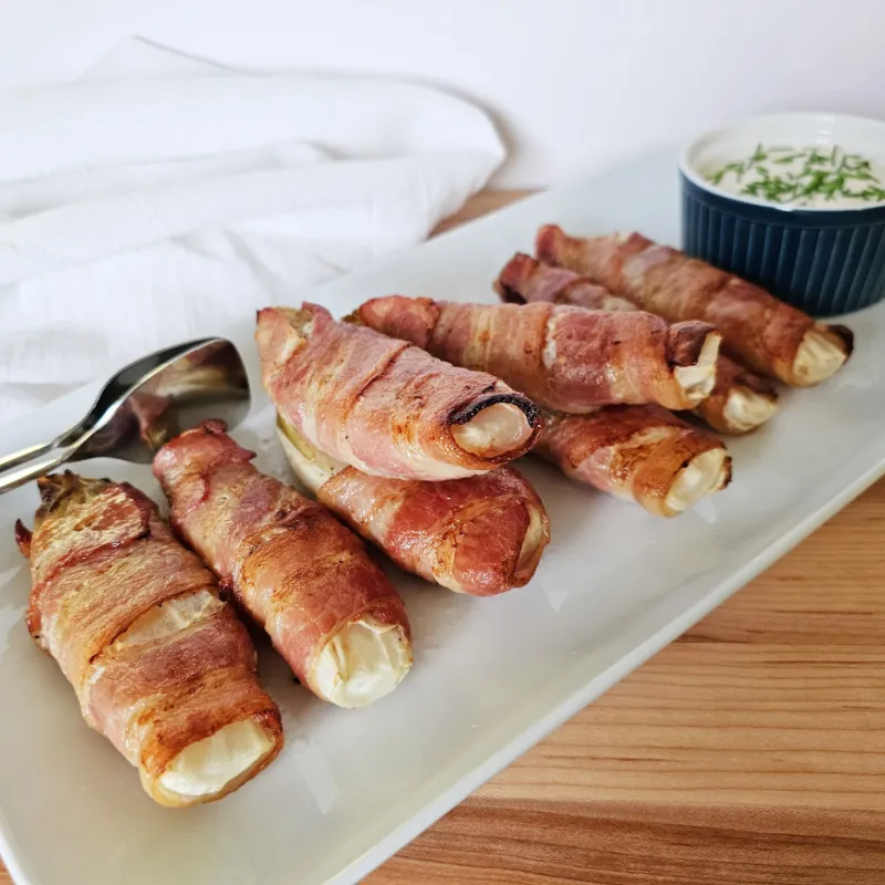 Bacon-wrapped Belgian endive served on a white platter with creamy mustard sauce and chives.
