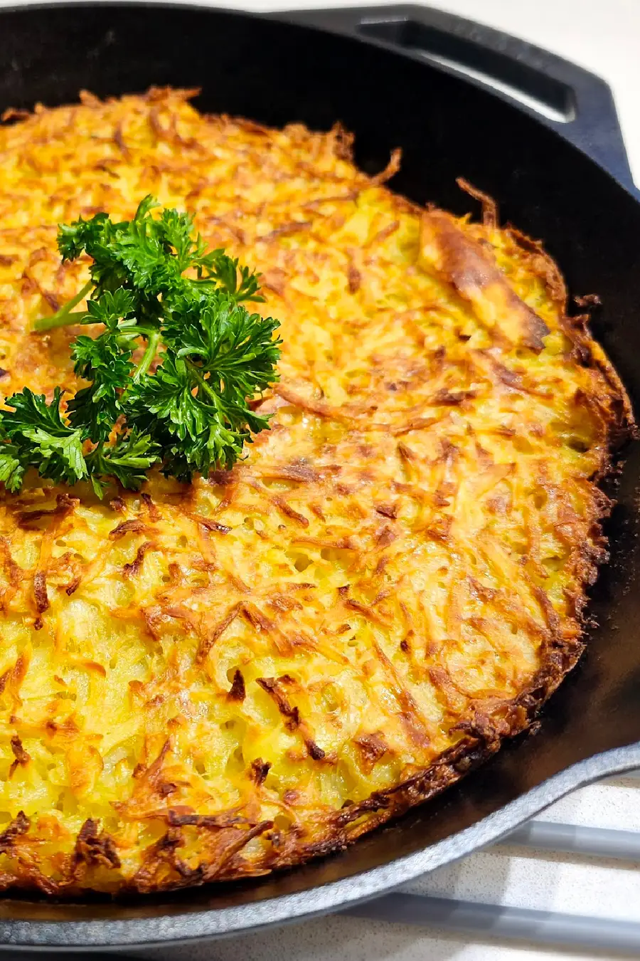 Oven Baked Potato Pancake Casserole (Kartoffelpuffer aus dem Ofen) in cast-iron skillet Kartoffelpuffer aus dem Ofen (baked German potato pancake casserole) baked in a cast-iron skillet with a crispy golden top and parsley garnish
