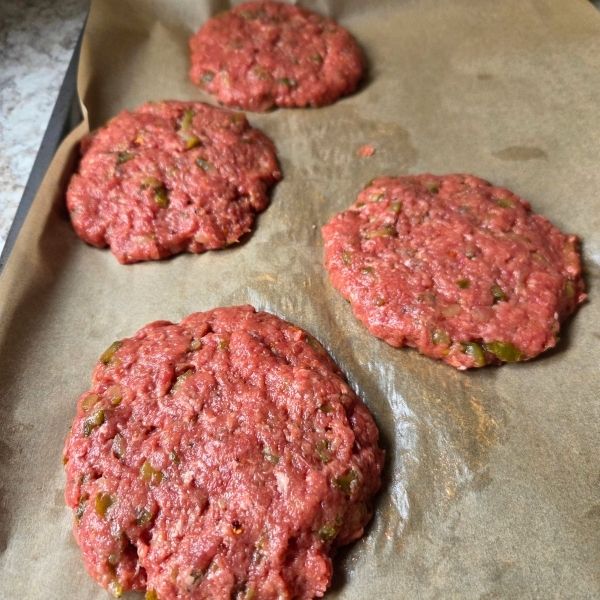 Burgers ready for grilling, sitting on a parchment-lined tray